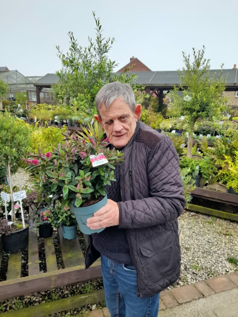 A service user holds up a plant to the camera, taken at Glapwell Garden Centre