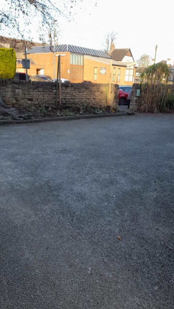 A clean and clear driveway with an even surface, framed by stone walls and greenery. The autumn sunlight casts a warm glow on the scene, showing a neat space free of leaves.