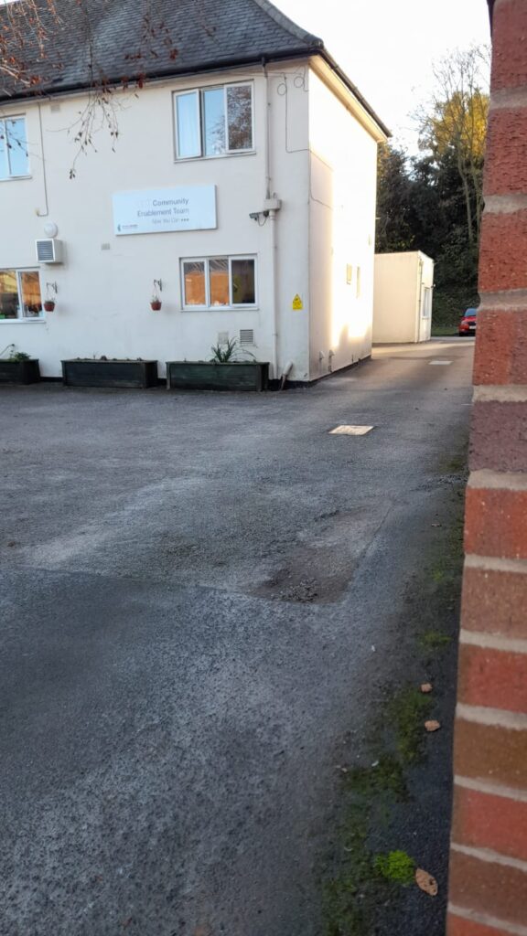 A section of the driveway near the Enablement Care building, with the building's sign visible on the wall. The driveway is clear of debris, showcasing a well-maintained outdoor space.