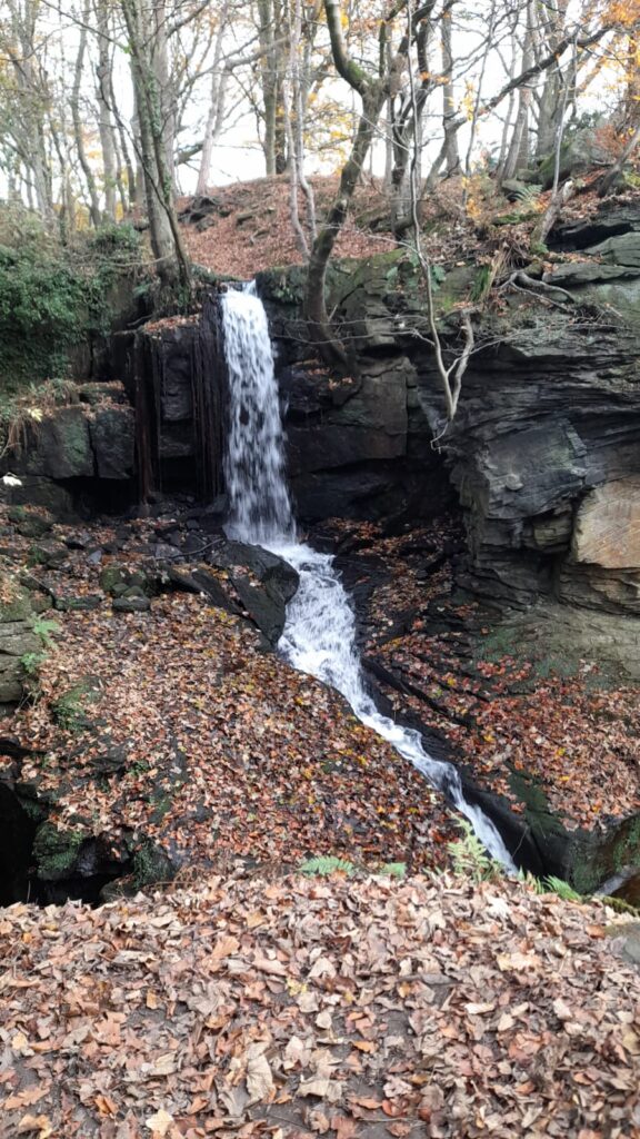 Waterfall among autumn leaves and rocks – A beautiful waterfall cascading down surrounded by rocky terrain and autumn leaves, capturing the natural beauty of the walking trail.