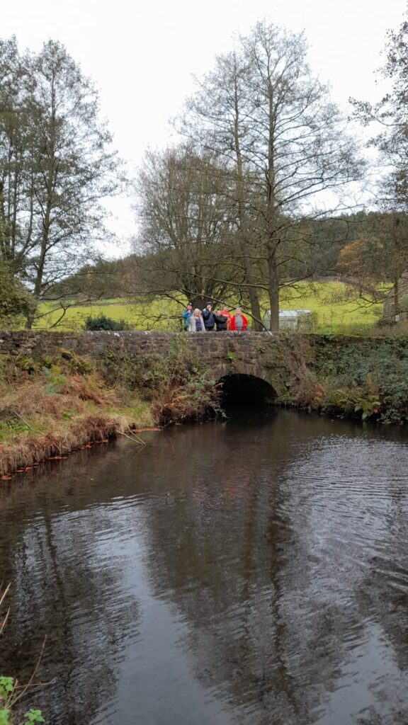 Walkers standing on a bridge by the river – Close-up of a group of walkers standing together on a stone bridge over a gentle river, enjoying the scenic surroundings.