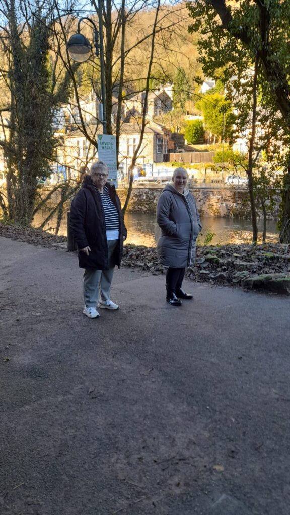 Two CET Walking Club members pause during the Lover’s Walk, framed by the tranquil riverside path and charming buildings in the background.