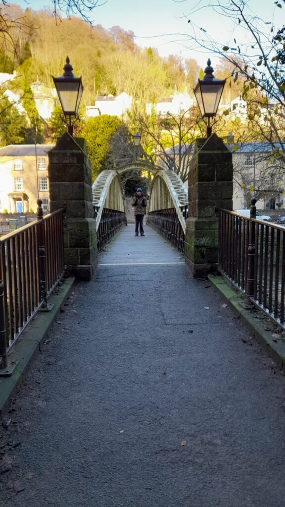 A wider view of Jubilee Bridge in Matlock, showcasing the picturesque architecture and a Walking Club member in the distance enjoying the scenery.