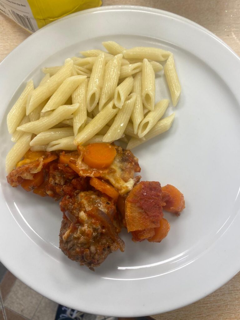 A plate of food featuring penne pasta served with meatballs in a rich tomato and vegetable sauce, topped with melted cheese.