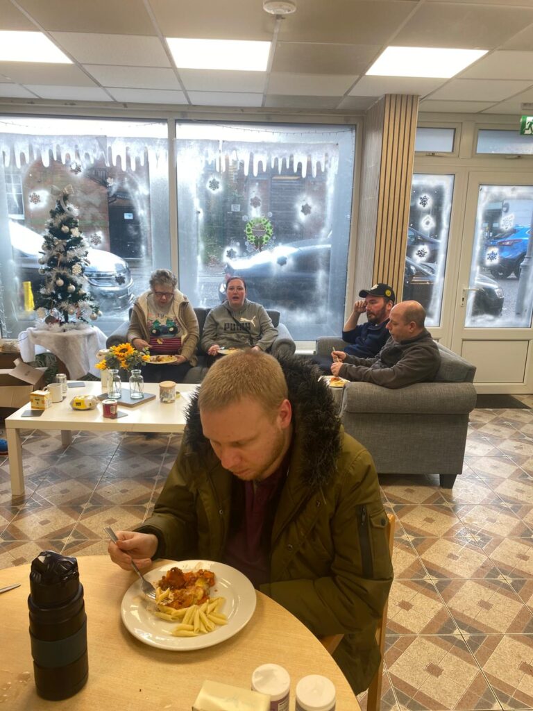 A group of people enjoying their meals in a cosy room with frosted winter-themed decorations on the windows and a small decorated Christmas tree in the background.