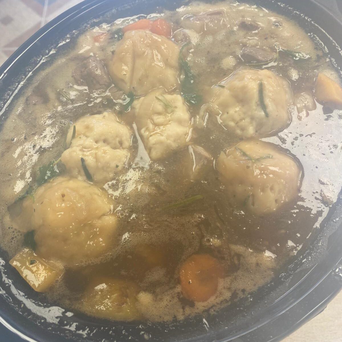 A steaming pot of lamb stew with large, golden dumplings floating on top, surrounded by chunks of carrots and vegetables in a rich broth.