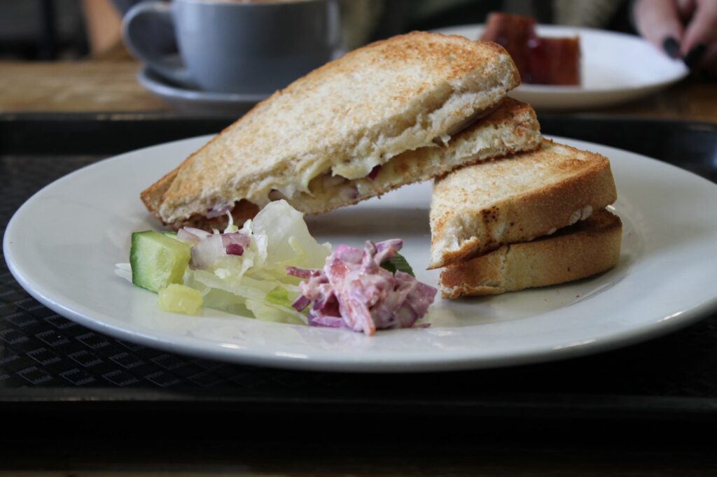 A close-up of a plate with a toasted sandwich, accompanied by fresh salad and coleslaw, served on a tray in a café setting.