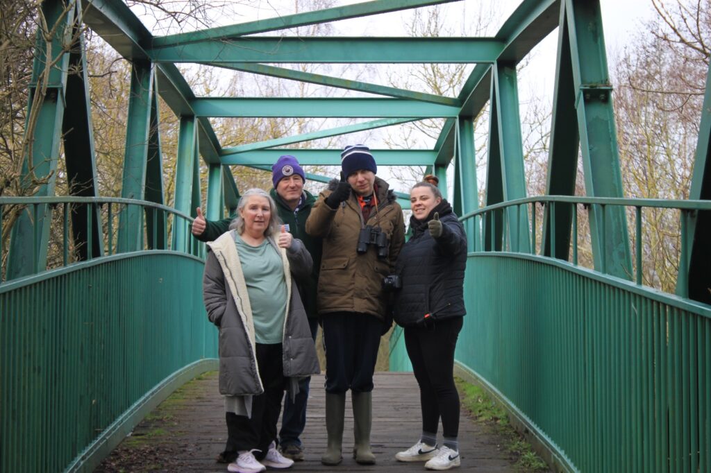 A group of four walkers posing on a green bridge, giving a thumbs-up to the camera.