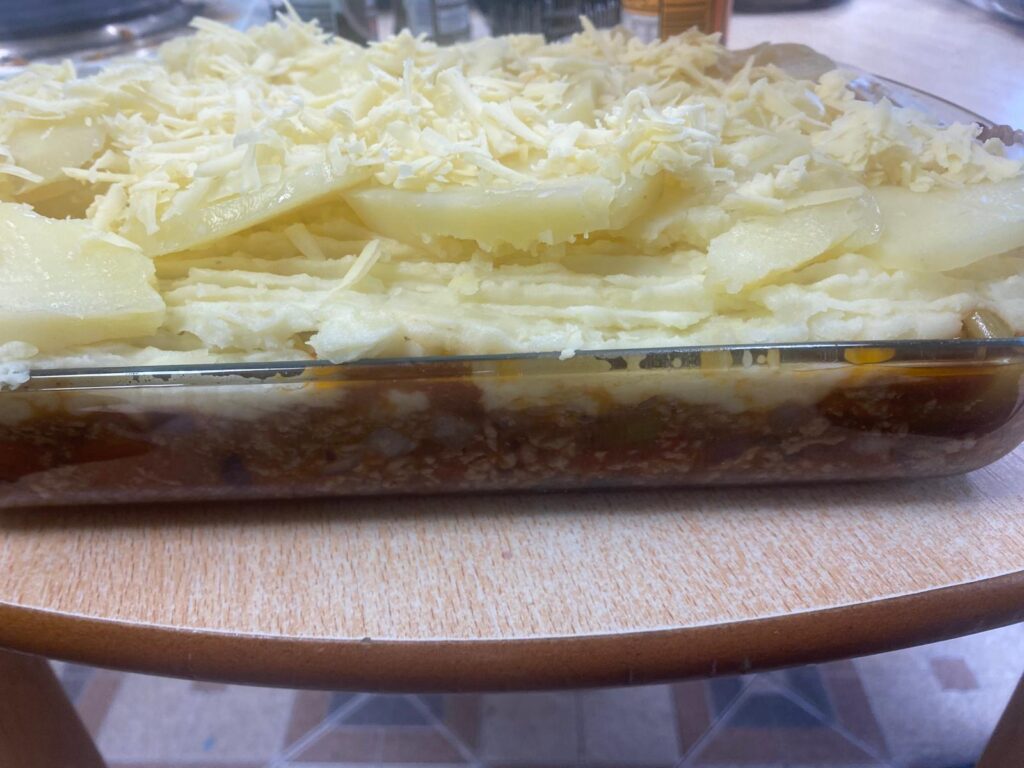 A glass dish filled with cottage pie, featuring a layer of mashed potatoes topped with grated cheese.