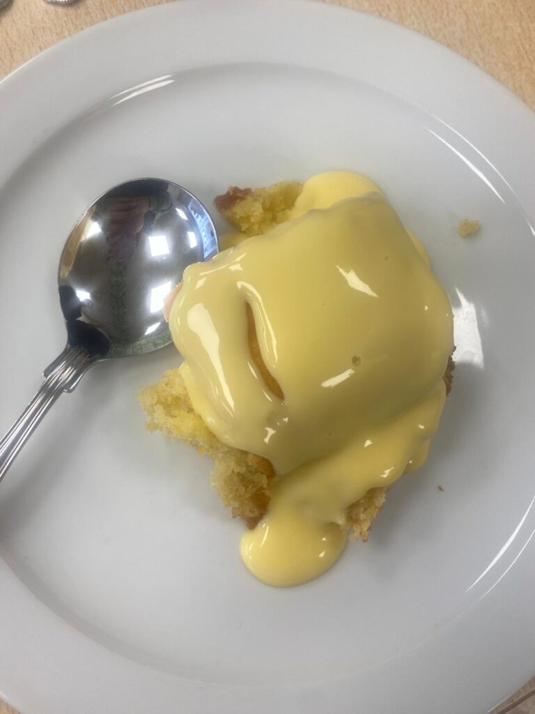 Close-up of a dessert plate featuring a slice of lemon sponge cake generously topped with custard.