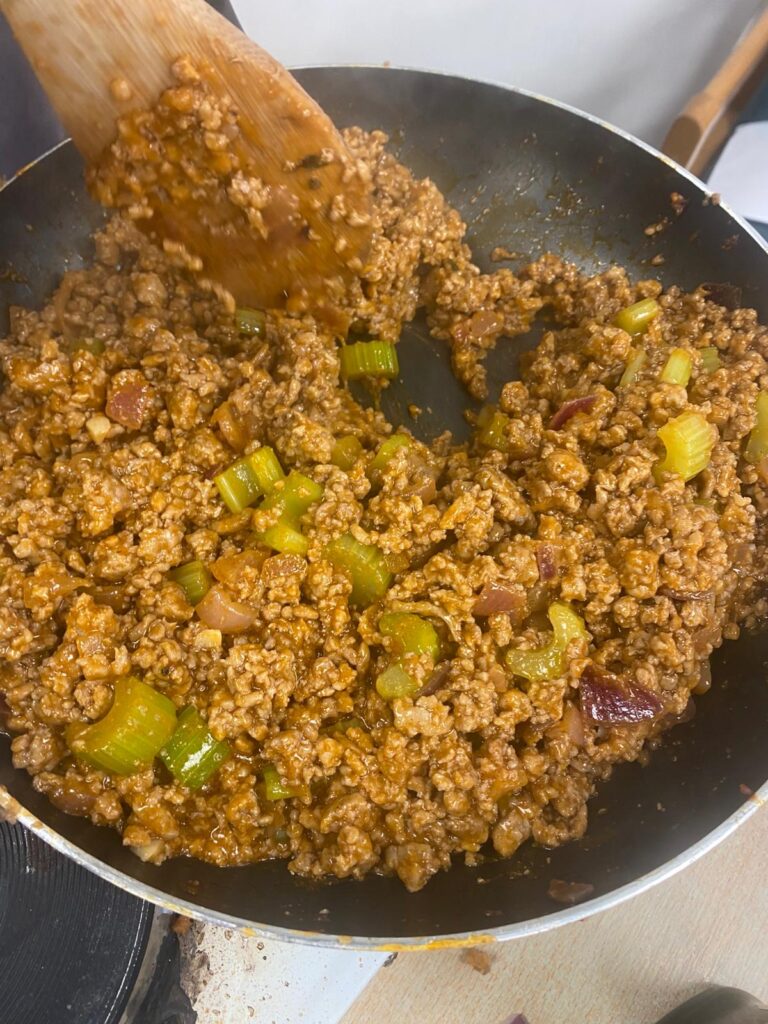 Close-up of minced meat and vegetables being stirred in a frying pan with a wooden spoon.