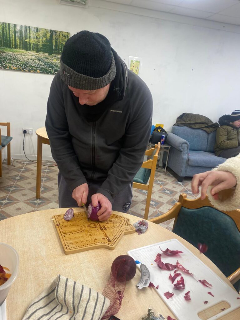 A man wearing a beanie carefully chopping a red onion on a decorative wooden chopping board.