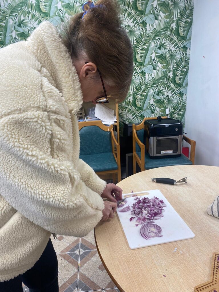 A person wearing glasses chopping red onions on a white chopping board, focused on their task.